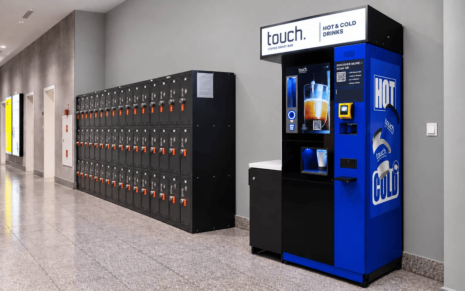 Vending machine for hot and cold drinks beside a wall of lockers