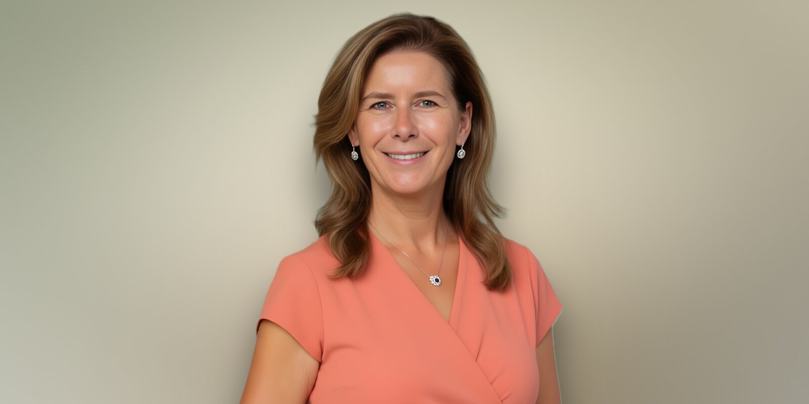 A woman in an orange shirt smiles warmly, embodying confidence and approachability in a professional setting.