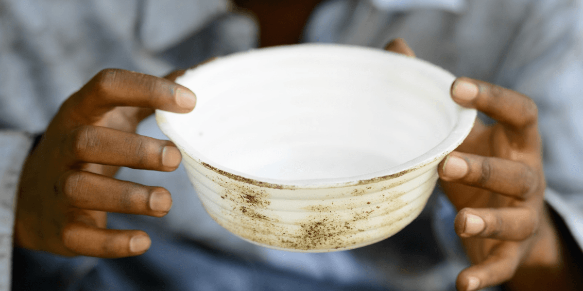 A person holds a dirty bowl, symbolizing the urgent need for food access and dignity, a core mission of Jasminica.