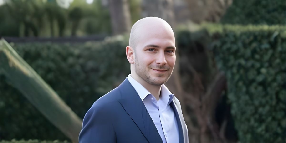 A bald man in a suit and tie smiles confidently, embodying professionalism and approachability in a corporate setting.