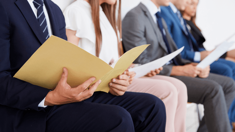 People sitting in a row holding documents, likely waiting for an interview.