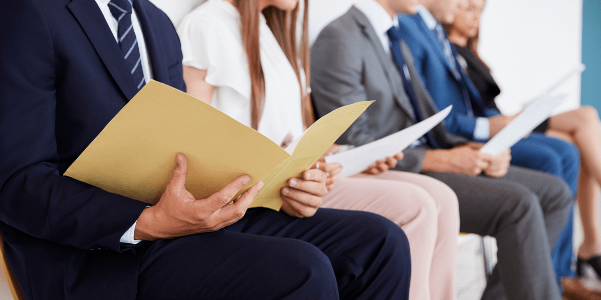 People sitting in a row holding documents, likely waiting for an interview.
