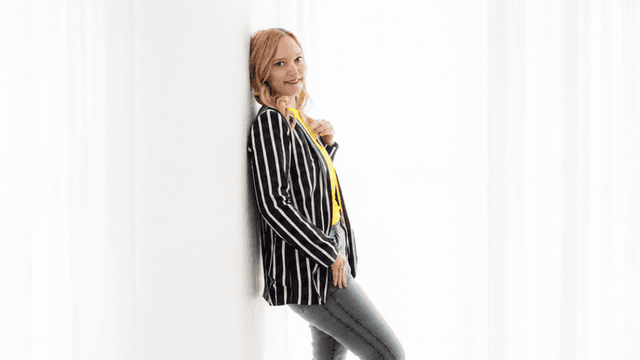 Woman in striped blazer and yellow top poses against a white backdrop