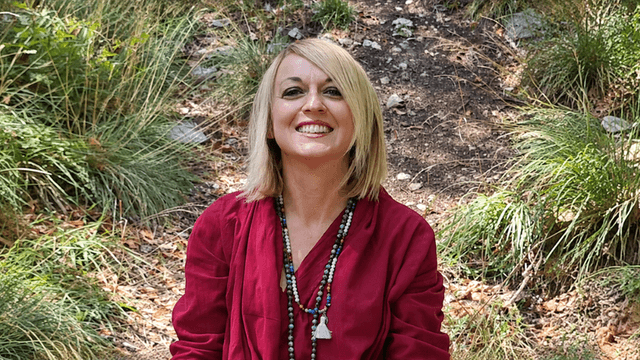 Smiling woman in a red outfit sitting in a natural, grassy outdoor setting