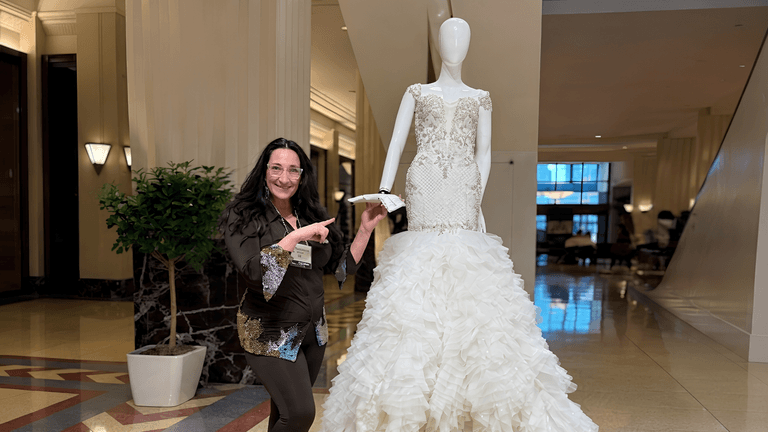 A woman poses beside a mannequin wearing an elegant ruffled wedding dress in a lobby