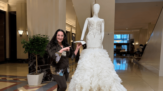 A woman poses beside a mannequin wearing an elegant ruffled wedding dress in a lobby