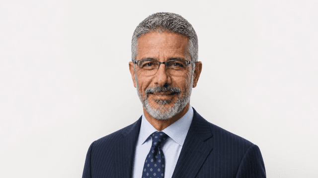Smiling middle-aged man in glasses, wearing a navy suit and patterned tie.