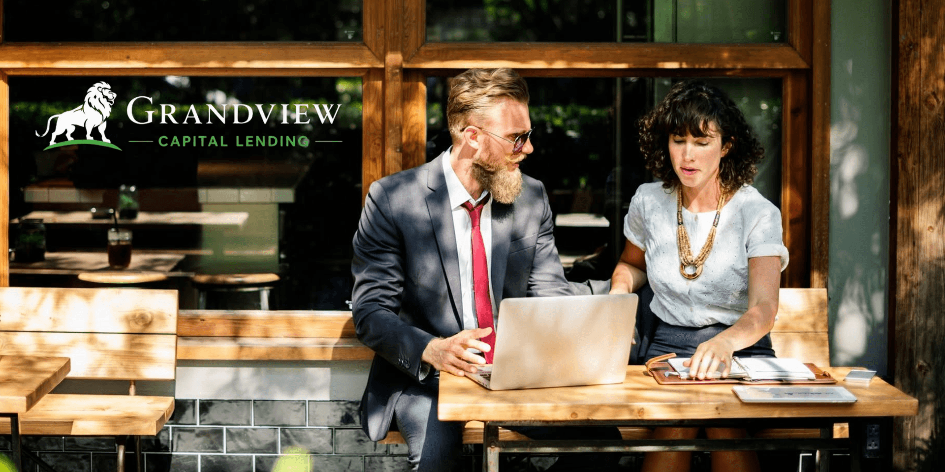 Two professionals discussing over a laptop at an outdoor café setting