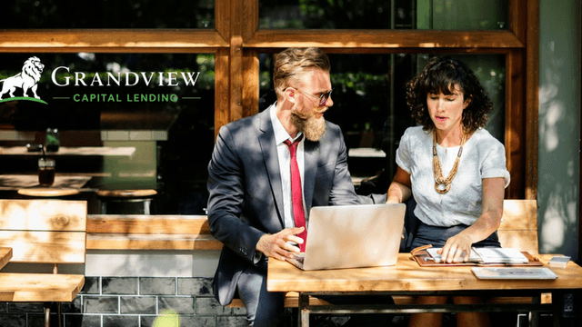 Two professionals discussing over a laptop at an outdoor café setting
