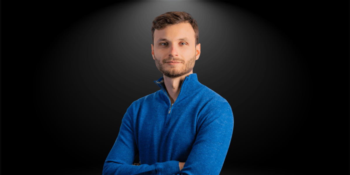 A young man wearing a blue sweater with arms crossed against a dark background