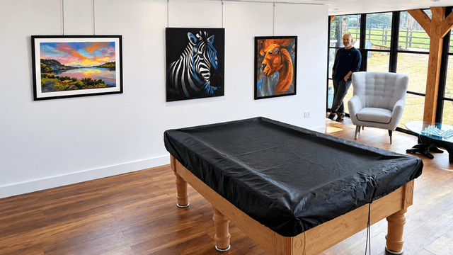 Art gallery interior featuring paintings of landscapes and animals with a billiard table