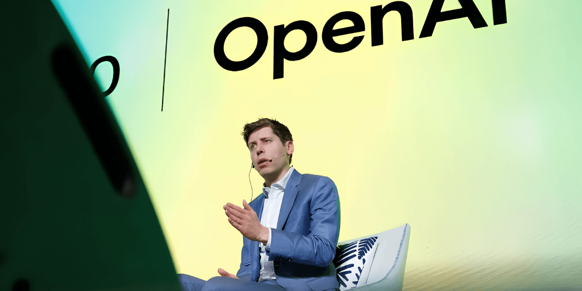 Person in a blue suit speaking on stage with OpenAI branding in the background