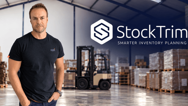 Man standing in a warehouse with inventory shelves and a forklift in the background