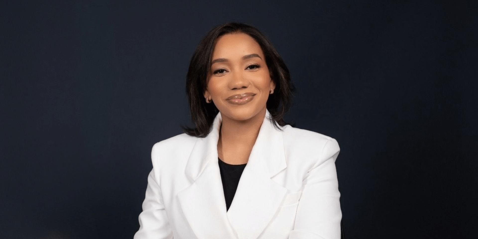 A professional woman in a white blazer smiles against a dark background