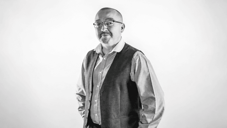 A man in a vest and shirt poses confidently against a light backdrop