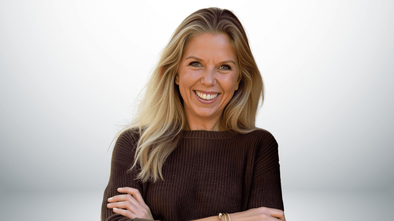 Smiling woman with long blonde hair wearing a brown sweater, arms crossed.