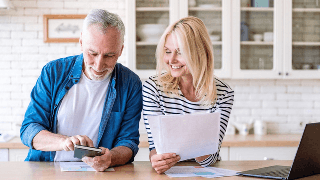 Smiling man and woman discussing documents at a kitchen table with a laptop nearby