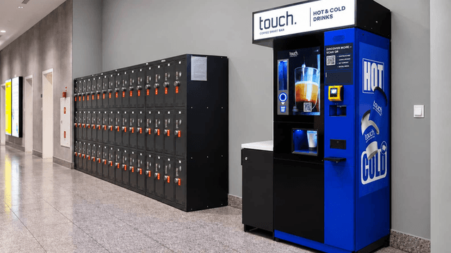 Vending machine for hot and cold drinks beside a wall of lockers