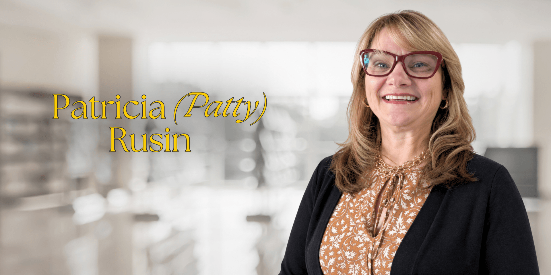 Smiling woman with glasses wearing a patterned blouse in a bright interior setting