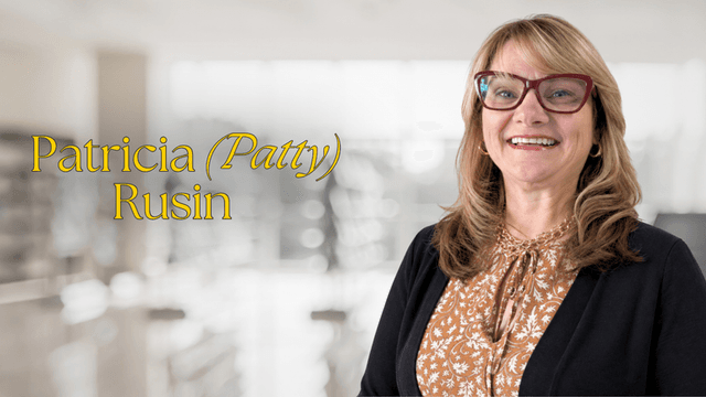 Smiling woman with glasses wearing a patterned blouse in a bright interior setting