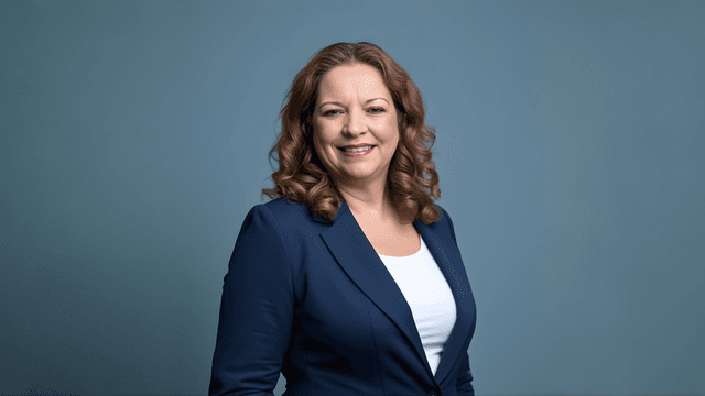 Smiling woman with curly hair wearing a blazer against a gray background