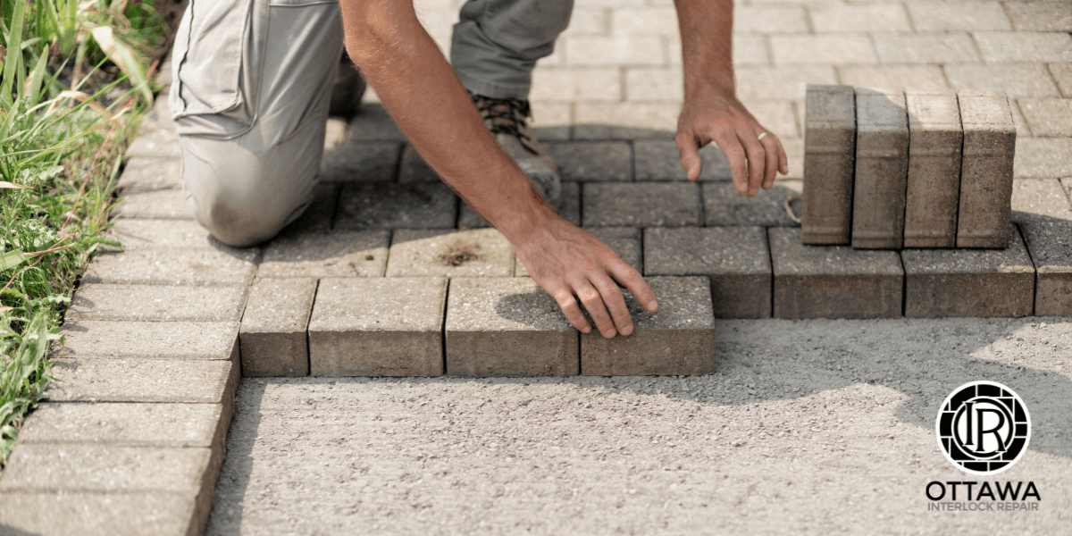A worker is carefully laying interlocking pavers on a surface for a landscaping repair project at Ottawa Interlock Repair.