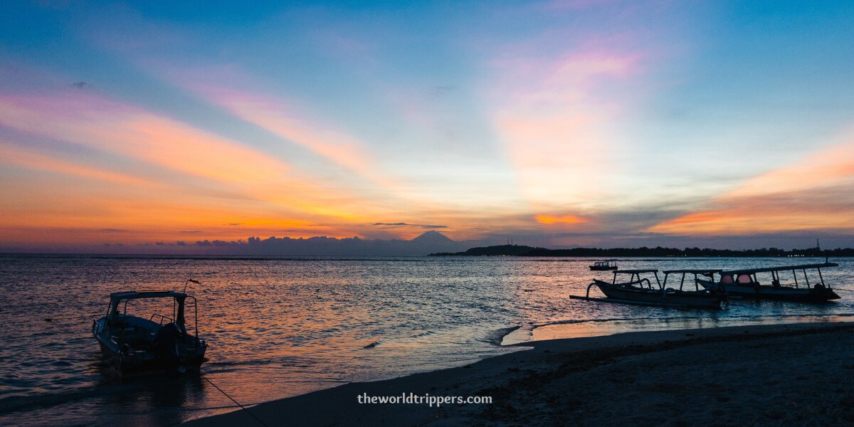 Sunset over Kuta Beach in Bali, showcasing vibrant orange and pink hues reflecting on the calm ocean waters.
