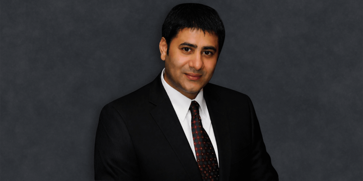 Professional man in suit and tie posing against dark studio background.
