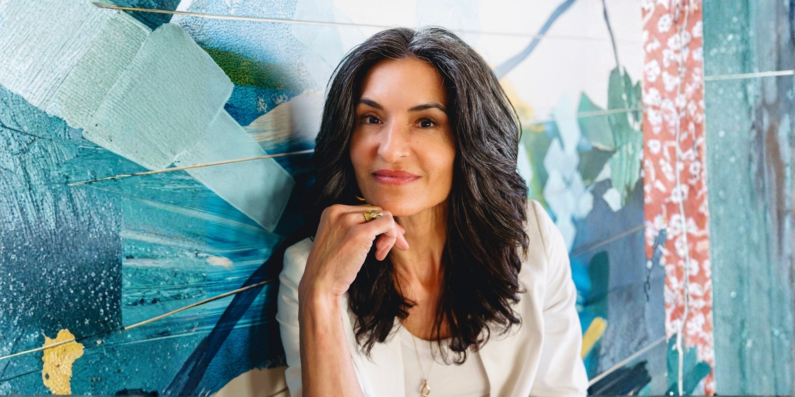 Jen Legaspi, a woman with long dark hair, sits thoughtfully against a colorful, abstract mural, embodying self-trust.