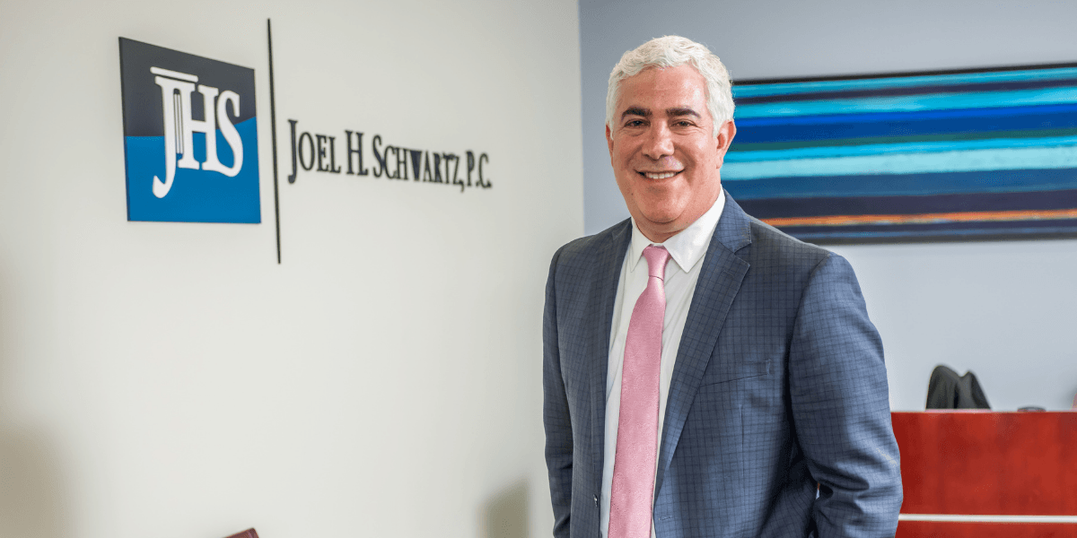 Steven A. Schwartz, in a blue suit and pink tie, stands in the office of Joel H. Schwartz, P.C.