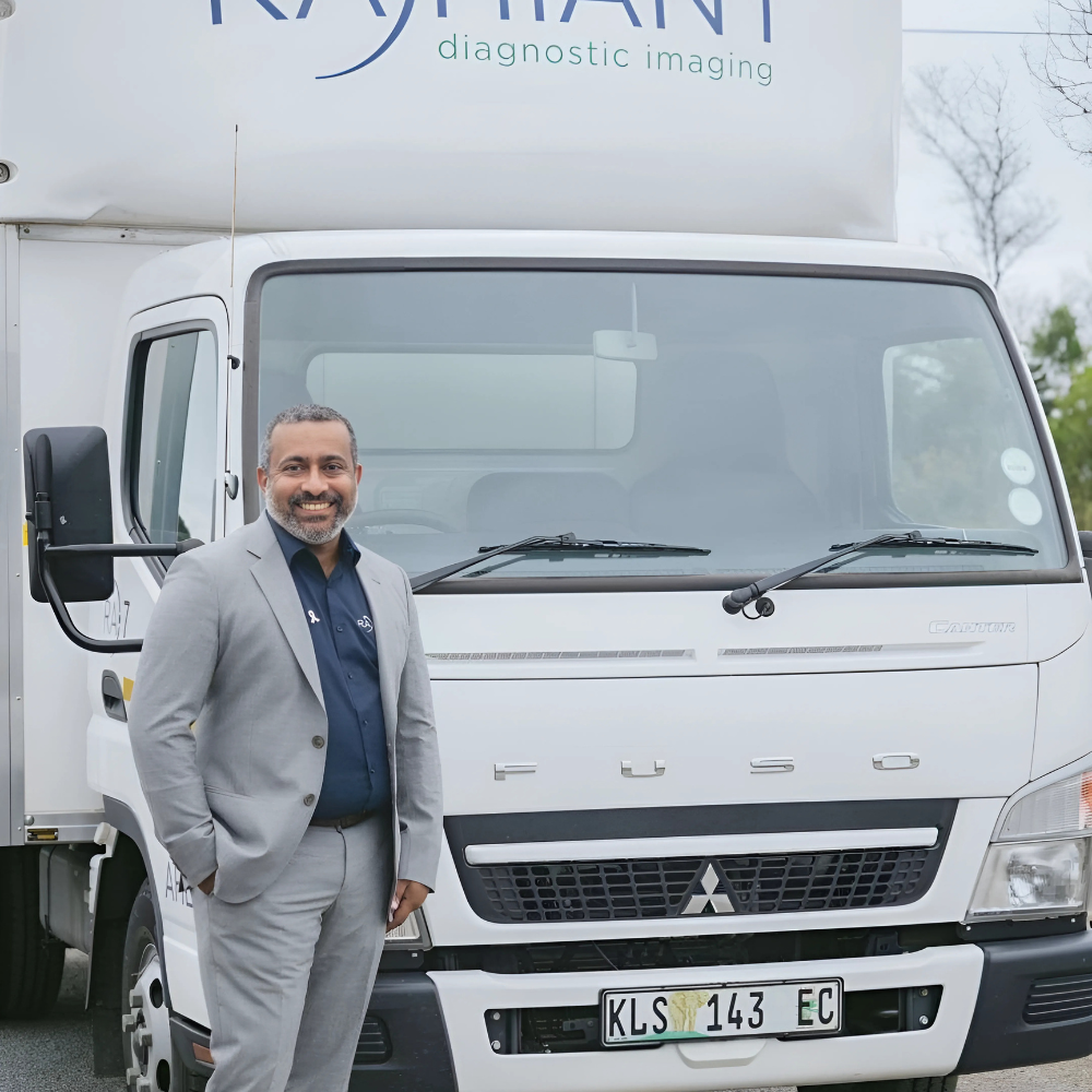 Man in a grey suit standing in front of a Mitsubishi truck with 'RAHIANT diagnostic imaging' written on the side.