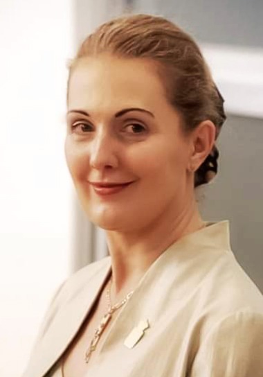 Close-up portrait of a woman with a subtle smile, wearing a light beige suit and a small pin, exuding a professional and confident demeanor