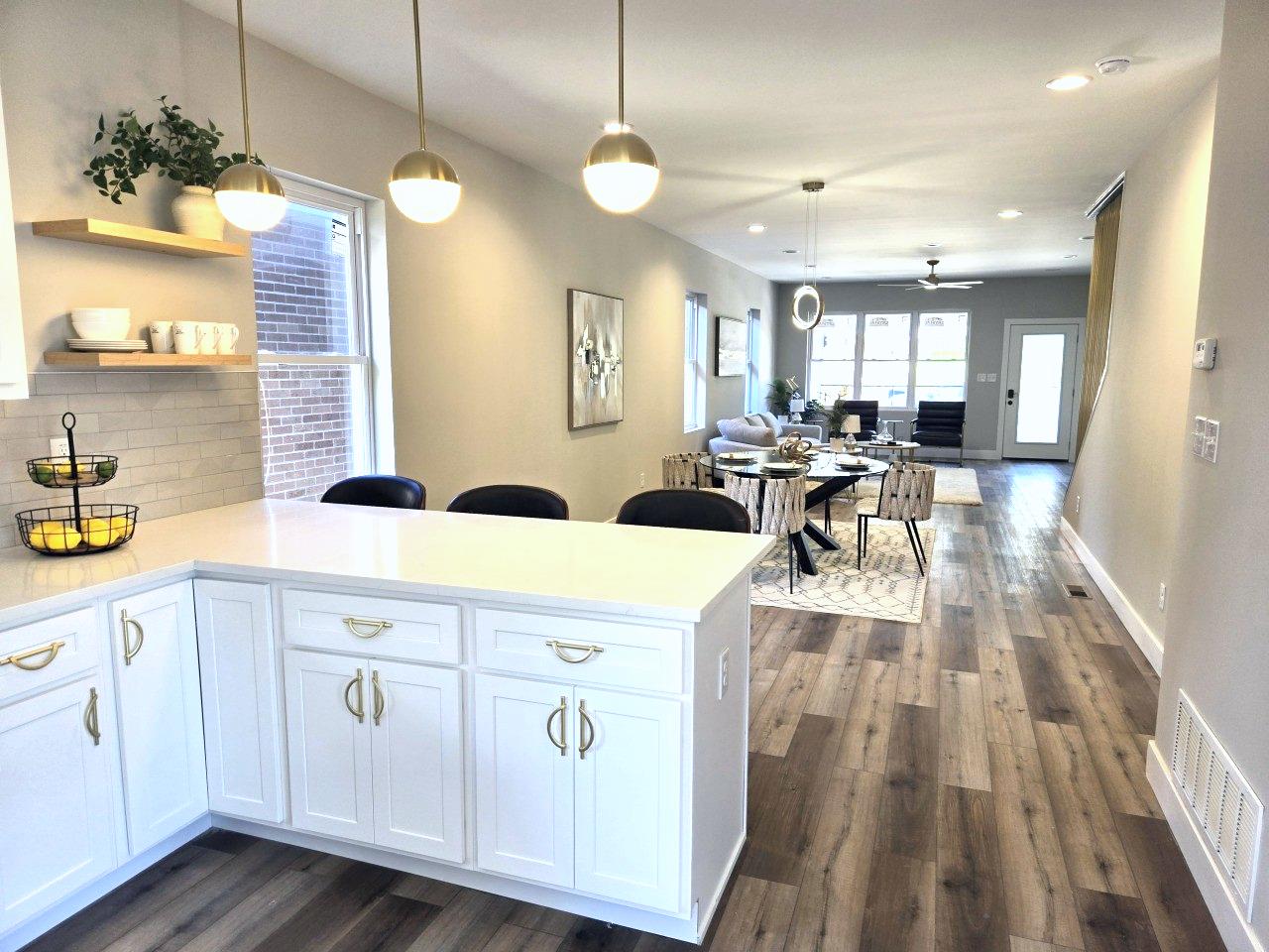 Bright, modern kitchen with white cabinetry, quartz countertops, and stylish pendant lights, overlooking a dining and living area with hardwood floors and contemporary furnishings.