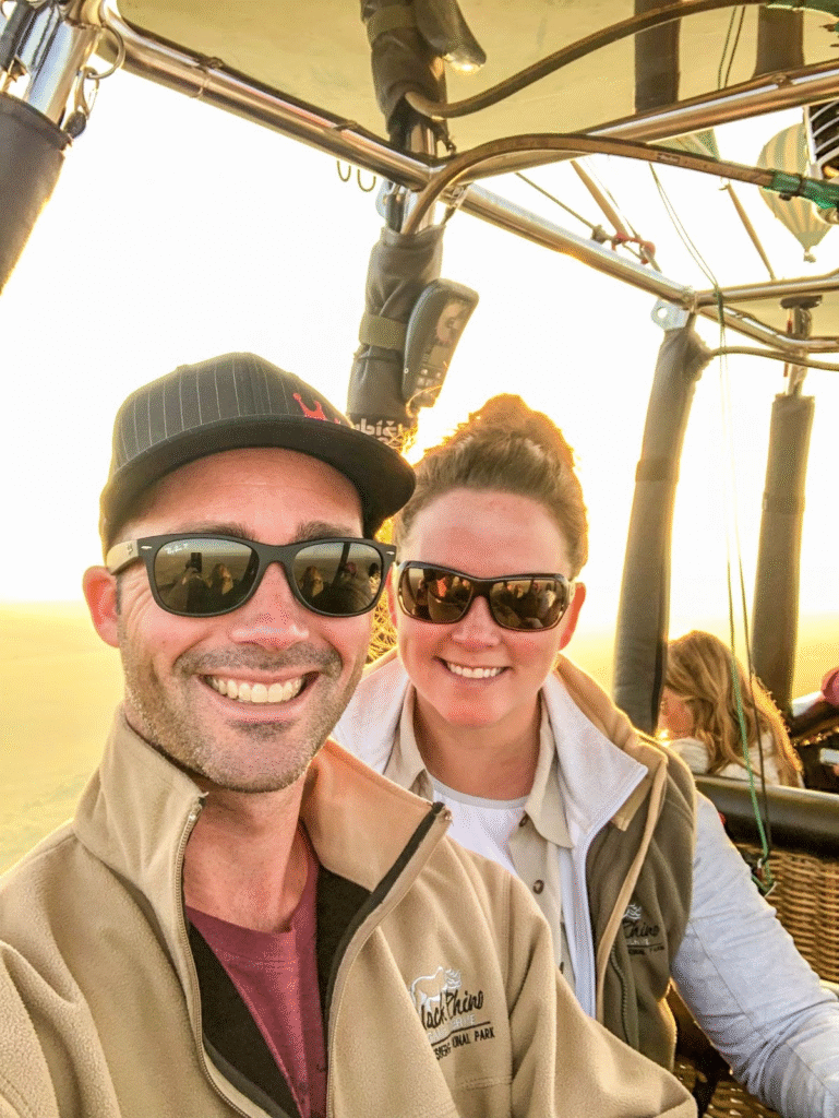 "Smiling couple enjoying a scenic hot air balloon ride at sunrise, wearing sunglasses and adventure jackets."