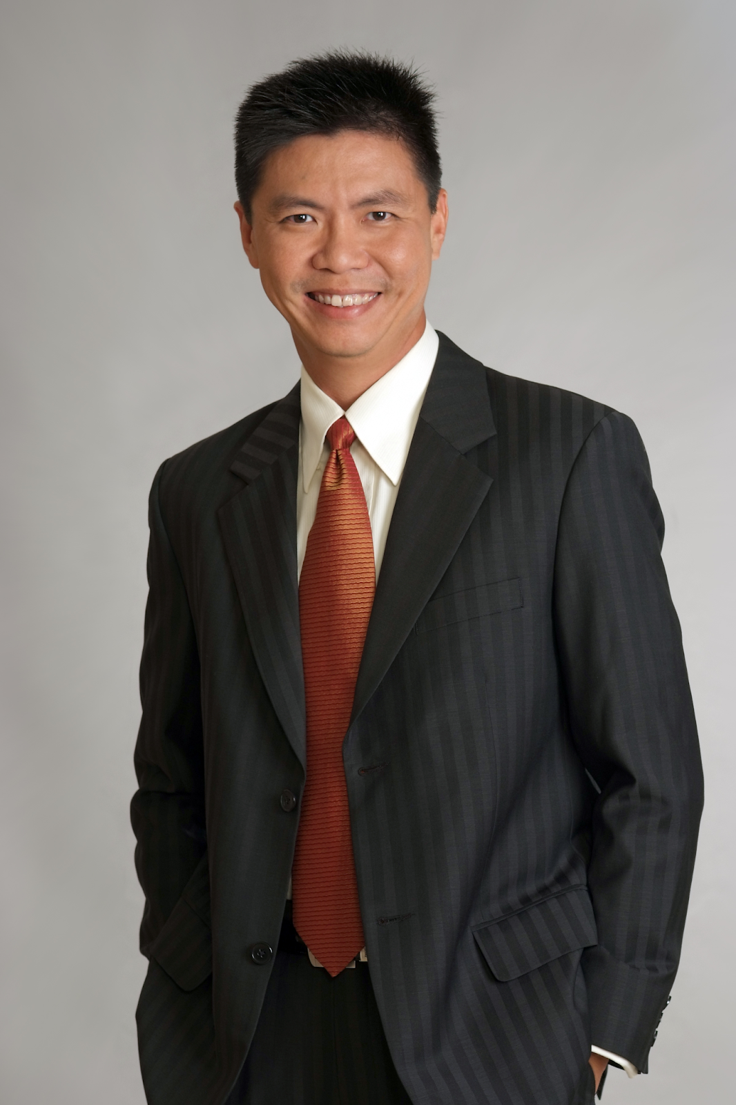 Portrait of a professional man in a black pinstriped suit with a red tie, smiling confidently against a neutral background