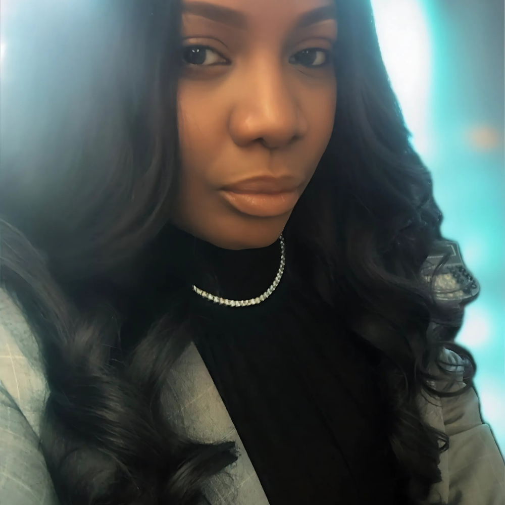 Self-portrait of Adyna K. Pressley, an empowered professional with long dark hair and a diamond necklace, capturing confidence and strength in a soft, glowing setting.