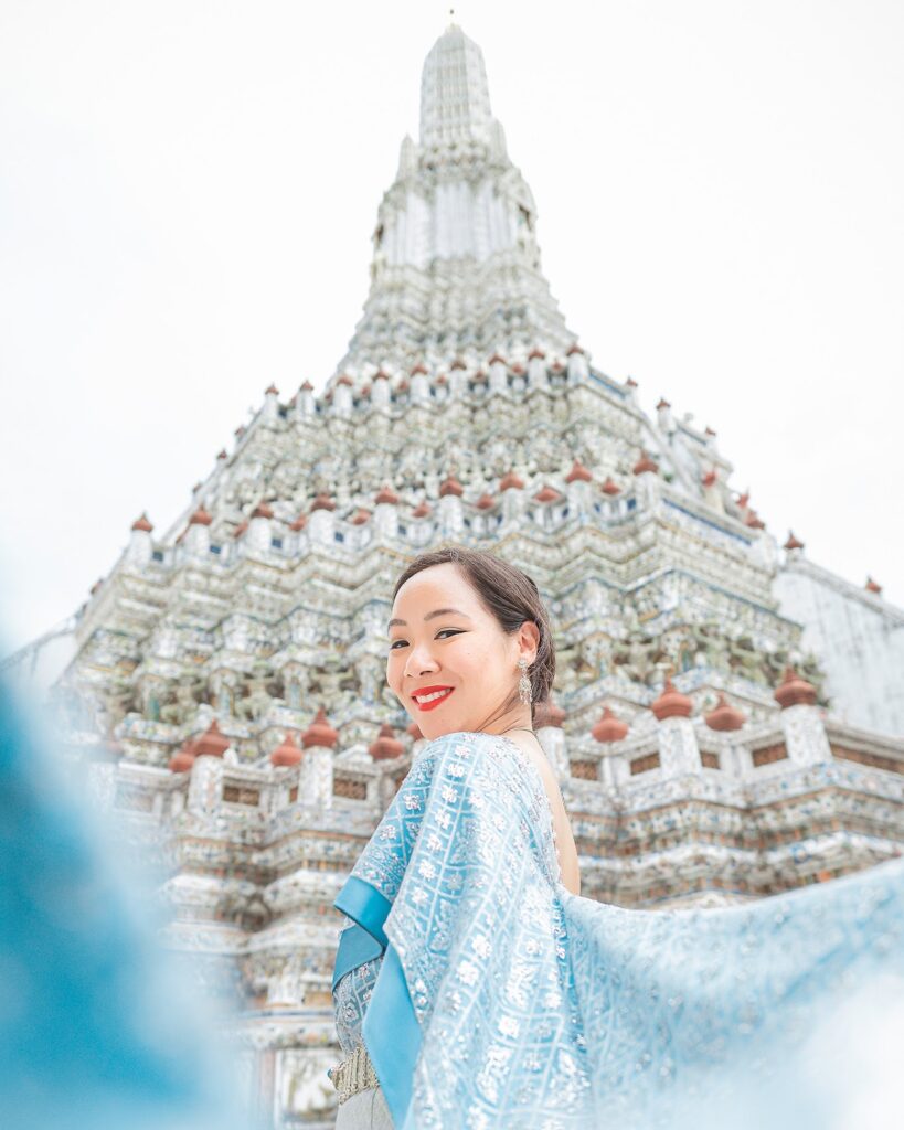 "Woman in a blue dress posing in front of the stunning Wat Arun temple in Bangkok, Thailand, showcasing cultural heritage and travel beauty."