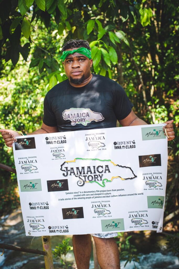 Man holding a promotional “Jamaica Story” banner in front of lush green foliage.