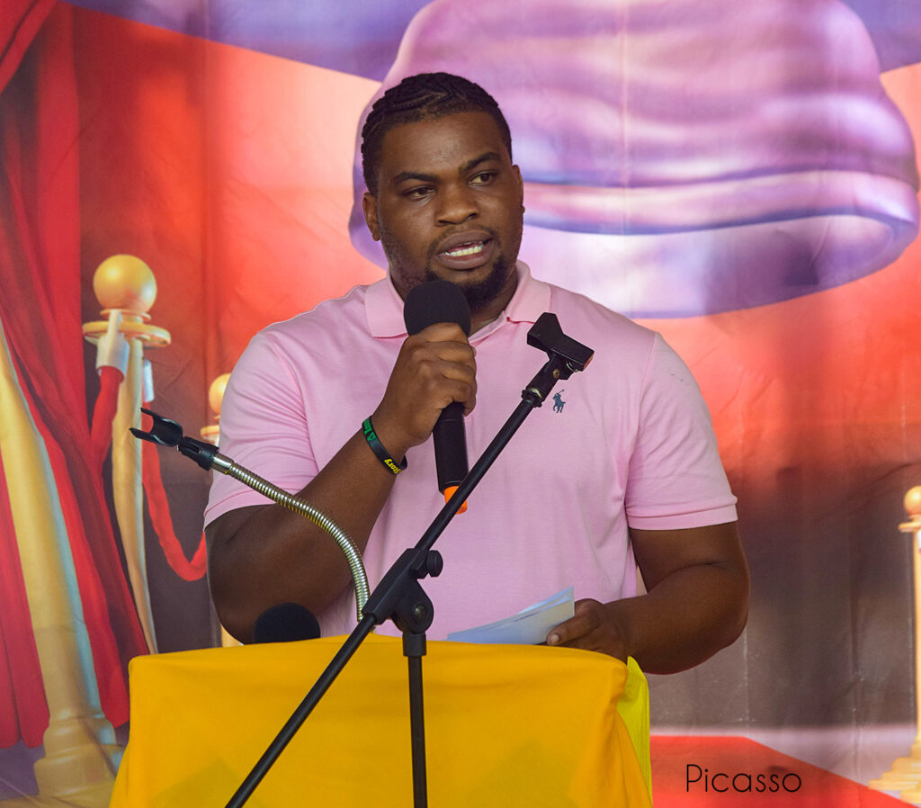 Man speaking into a microphone at a podium with a colorful backdrop.