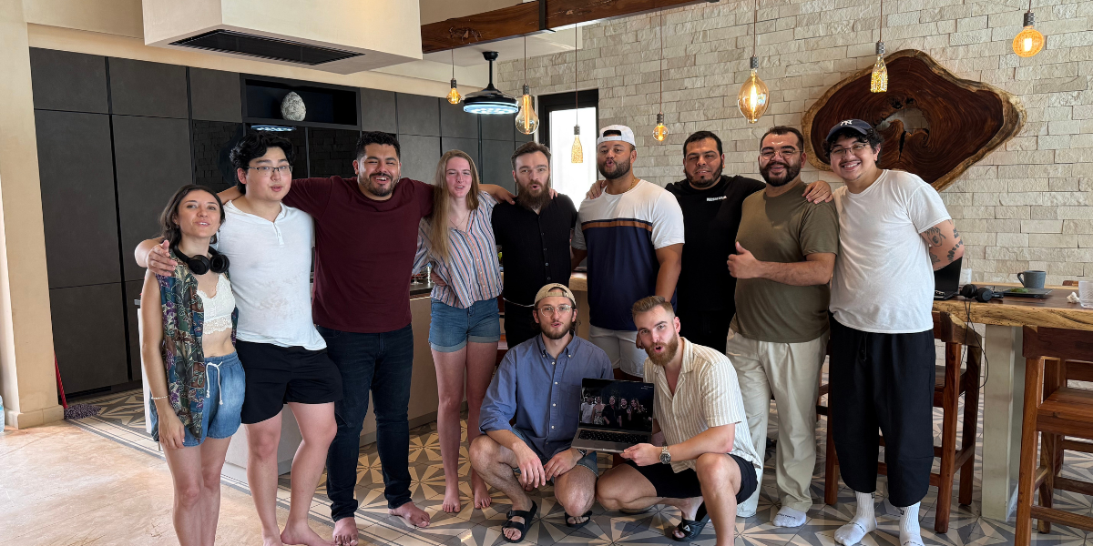 Group photo of a diverse team of individuals standing and sitting together in a modern interior, smiling and posing with a laptop in a relaxed atmosphere.
