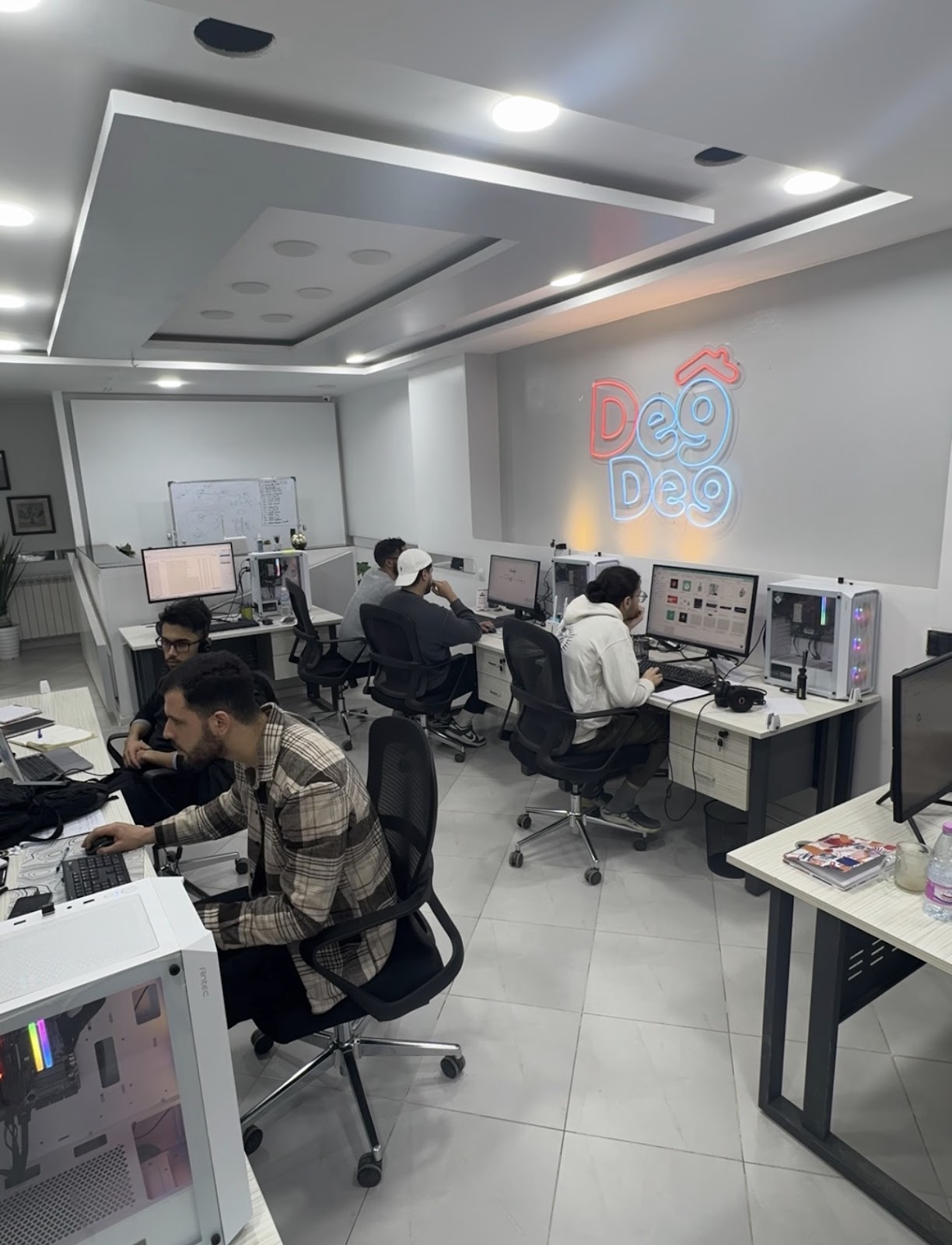 A modern office space with employees working at their desks, featuring computers and the DegDeg company logo illuminated on the wall.