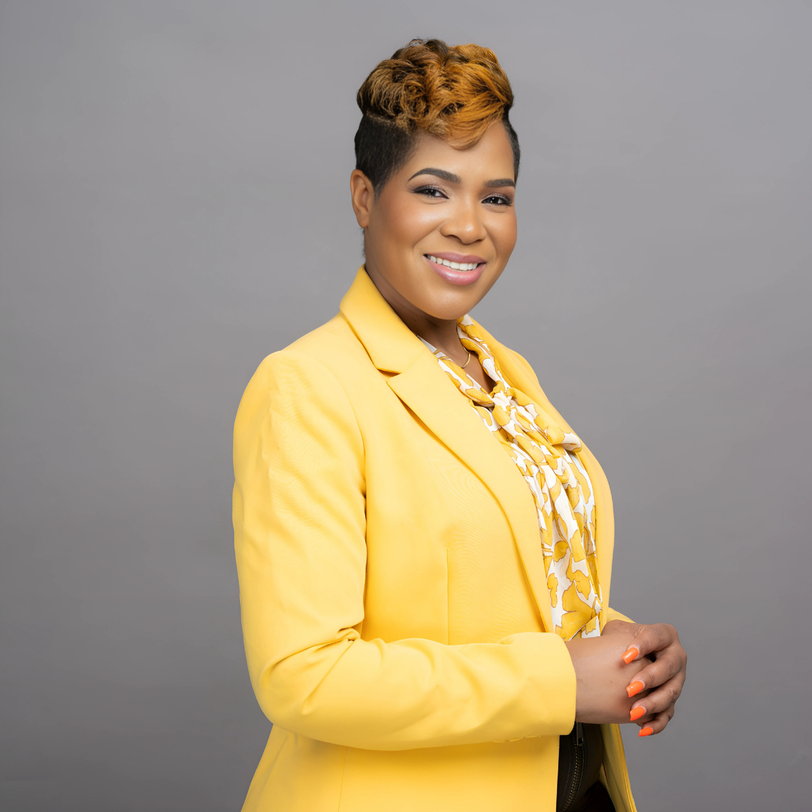 Portrait of a woman in a yellow suit smiling warmly, exuding confidence and professionalism in a studio setting."