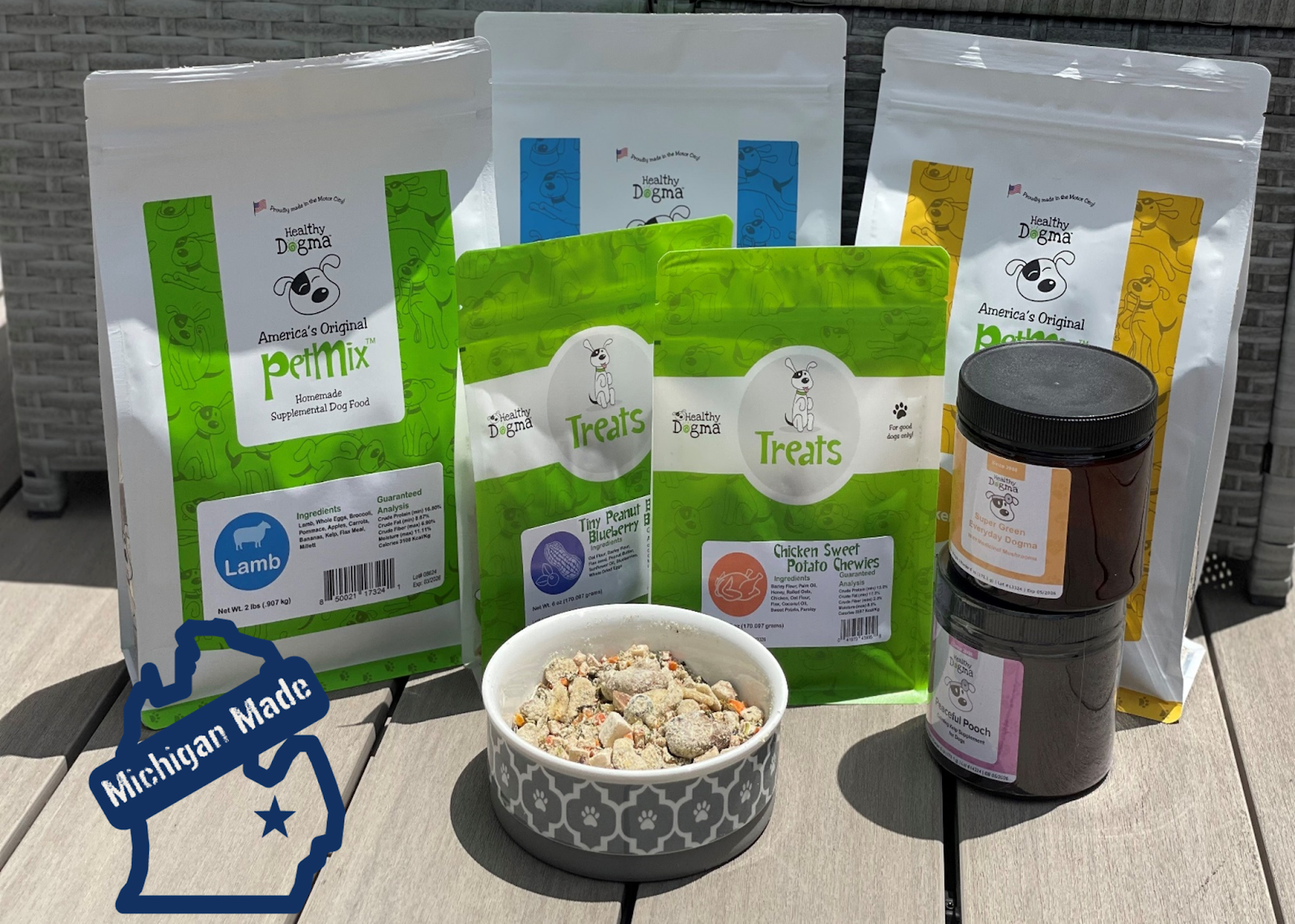 Healthy Dogma pet food products including PetMix, treats, and supplements for dogs, featuring Michigan-made labels and a bowl of mixed food ready for serving.