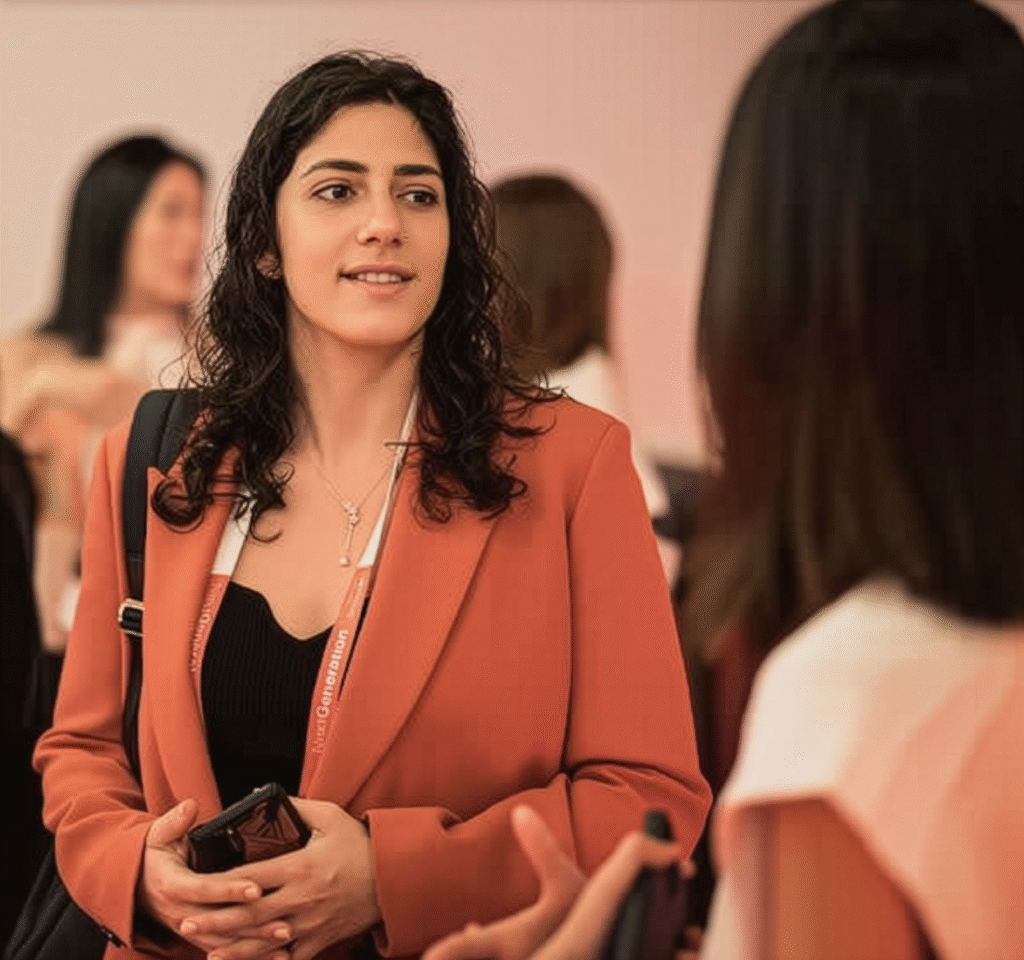 Margot Duek in an orange blazer, networking at an event, holding a phone and engaging with others