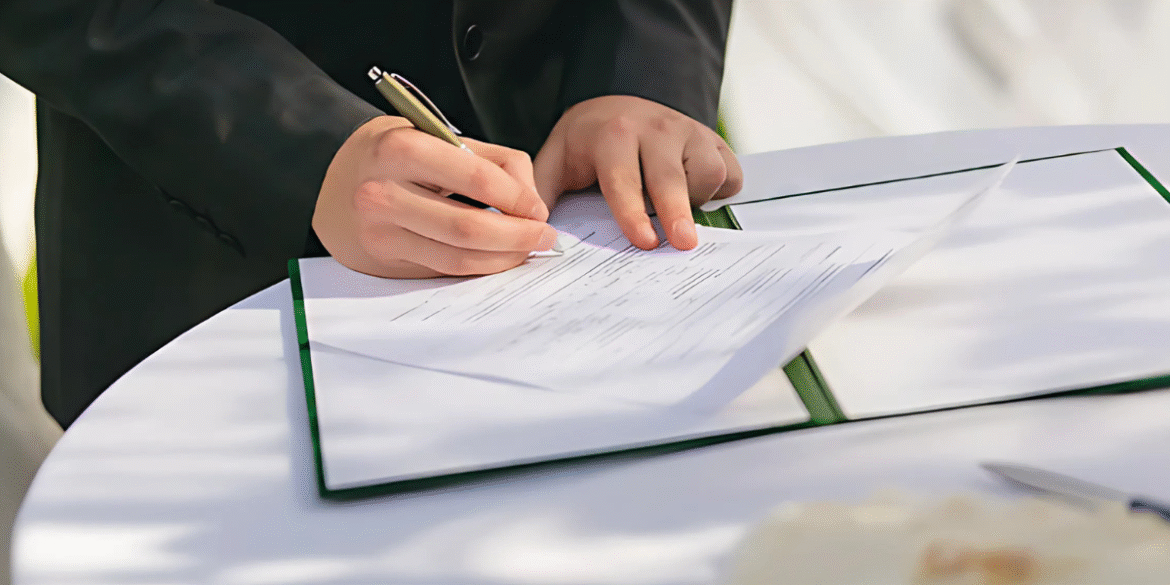 Person signing official documents on a table, representing post-license support at California Dealer Academy.