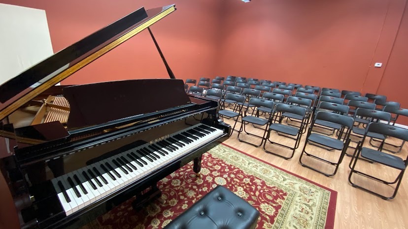 White Kawai grand piano on display in showroom surrounded by other grand pianos for sale.