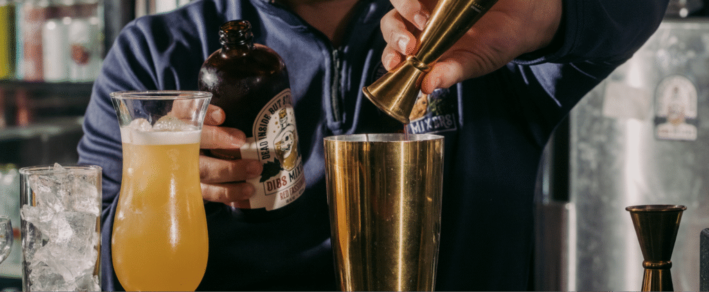 Bartender pouring Red Fassionola syrup into a cocktail shaker.