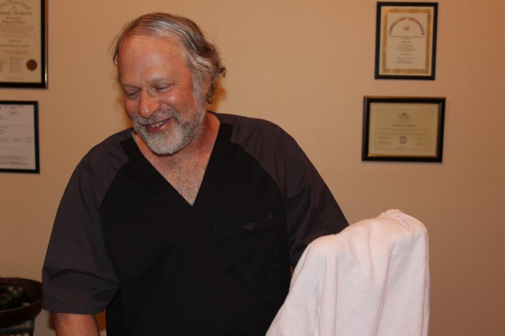 Andrew Scheim smiling in a therapy office, representing his expertise in PEMF and holistic bodywork therapies.