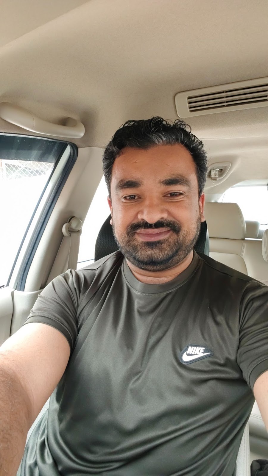 Malik Umar Awan smiling in a car, wearing a Nike t-shirt.