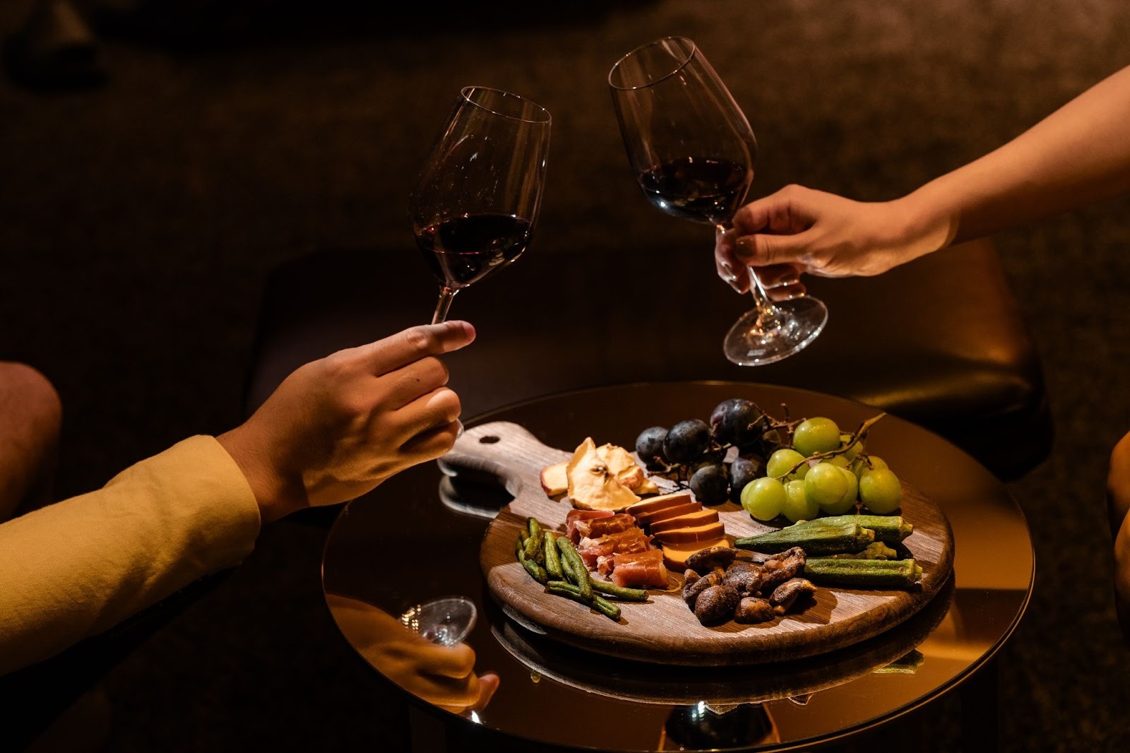 Toasting wine glasses over a Twelvita snack platter with fresh fruits, vegetables, and dried snacks.